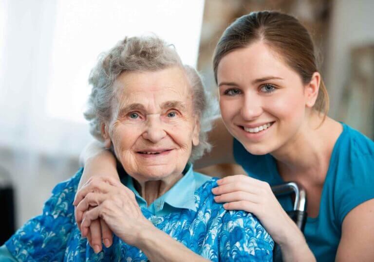 A nurse in scrubs standing beside a hospice inpatient lying in a hospital bed, offering comfort and care.