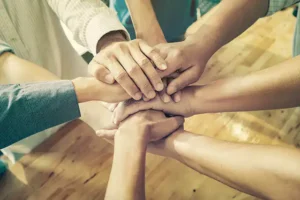 Several hands of diverse individuals joined together in a circle, symbolizing unity and grief support.