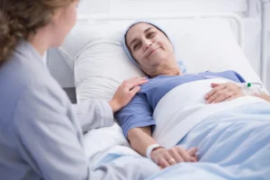 Hospice patient with skin cancer resting in bed, being comforted by a visitor.