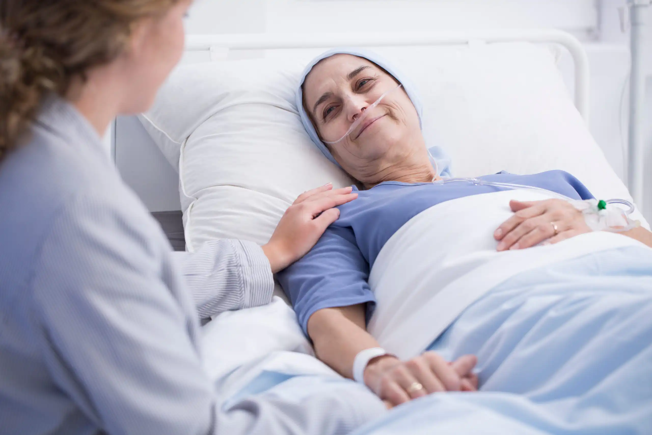 Hospice patient with skin cancer resting in bed, being comforted by a visitor.